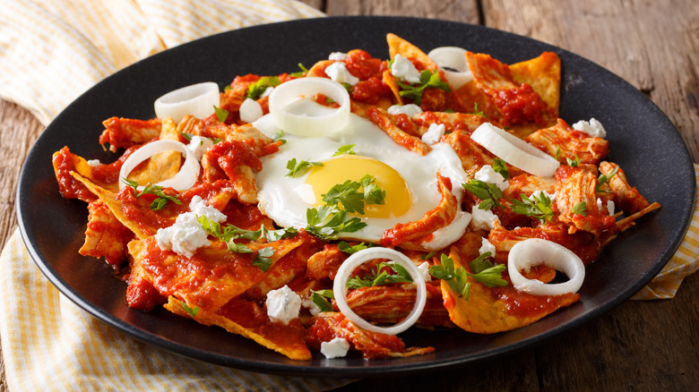 Black plate with red chilaquiles with egg on top