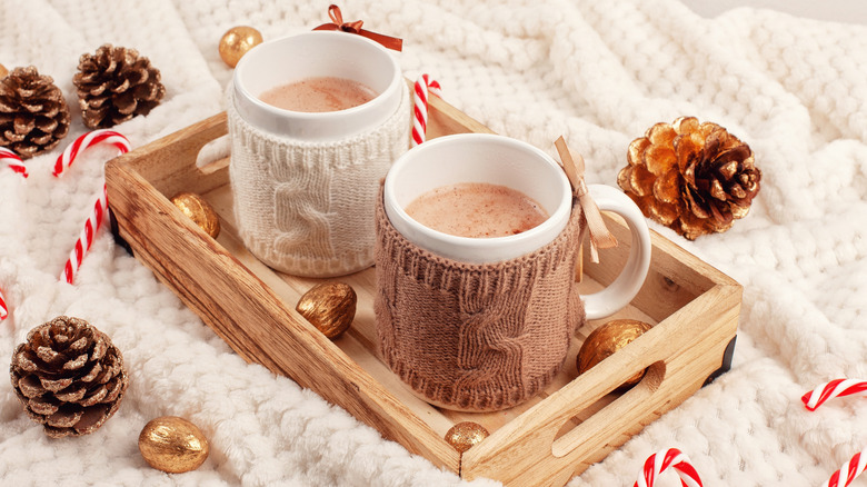 Two mugs of hot chocolate on a white tray with pinecones and candy canes around it