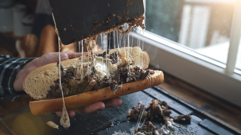 Hand scooping steak and cheese onto a sandwich roll